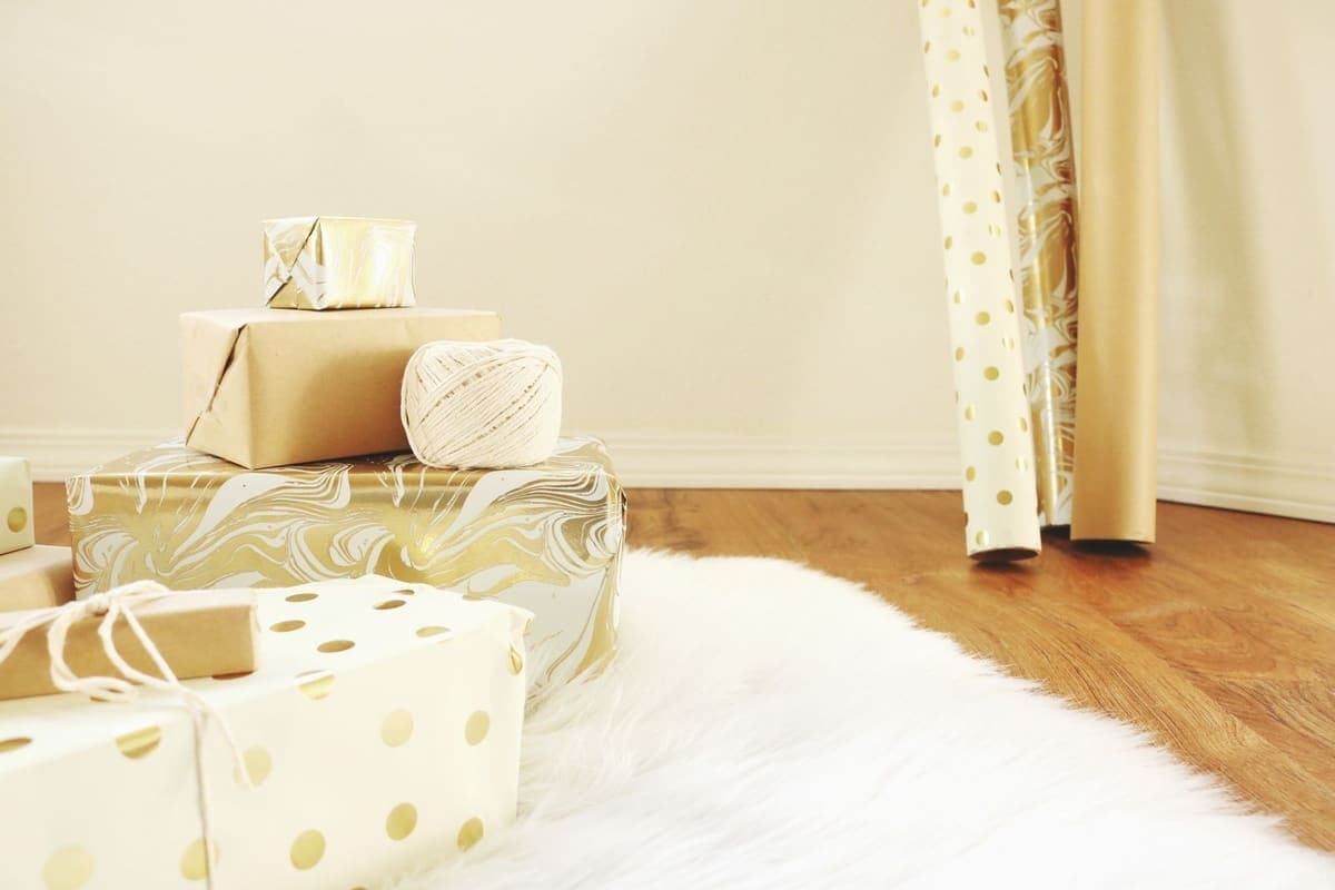 A stack of wrapped gifts in gold and white paper on a wooden floor in daylight